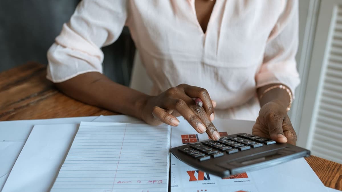 Mãos usando calculadora ao lado de caderno com anotações de custo