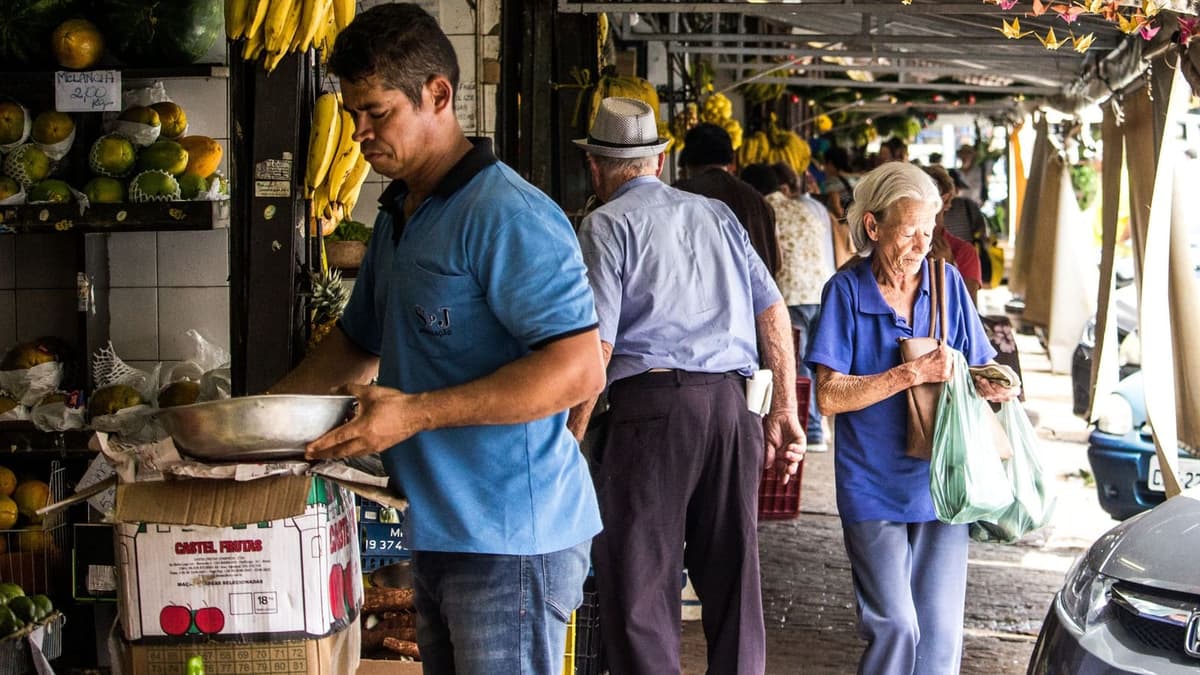 Vendedor de feira atendendo dois clientes na banca de frutas