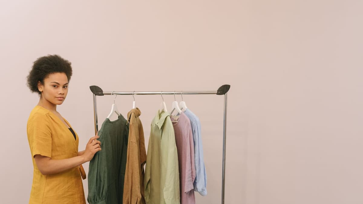Arara com peças de roupa em cabides diante de parede lisa