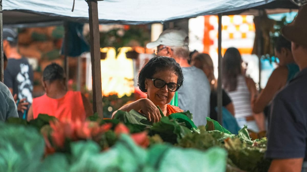 Feirante sorrindo atrás da banca de verduras, em feira livre brasileira