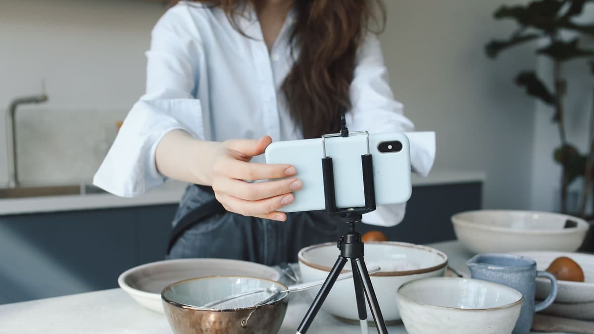 Mãos ajustando o celular num tripé de mesa para filmar produtos